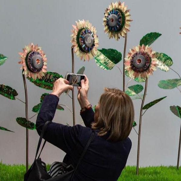 Person taking a photo of sunflower-shaped sculptures with a smartphone.