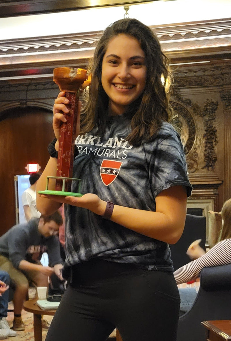 Person holding a circuit board trophy in a room with ornate decor and people in the background