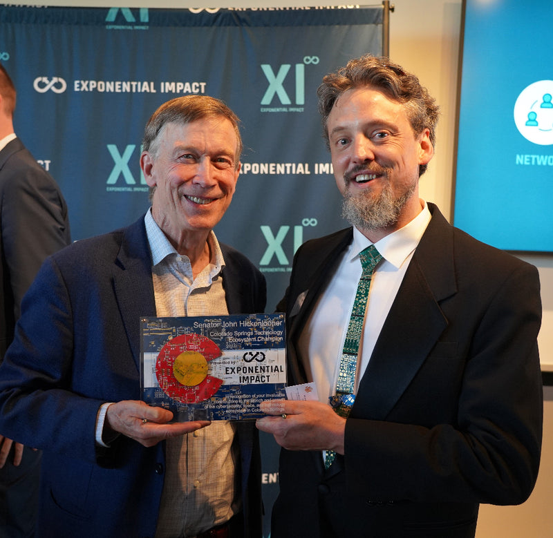 Two men in suits standing next to each other, holding a Colorado Flag Circuit Board Award.